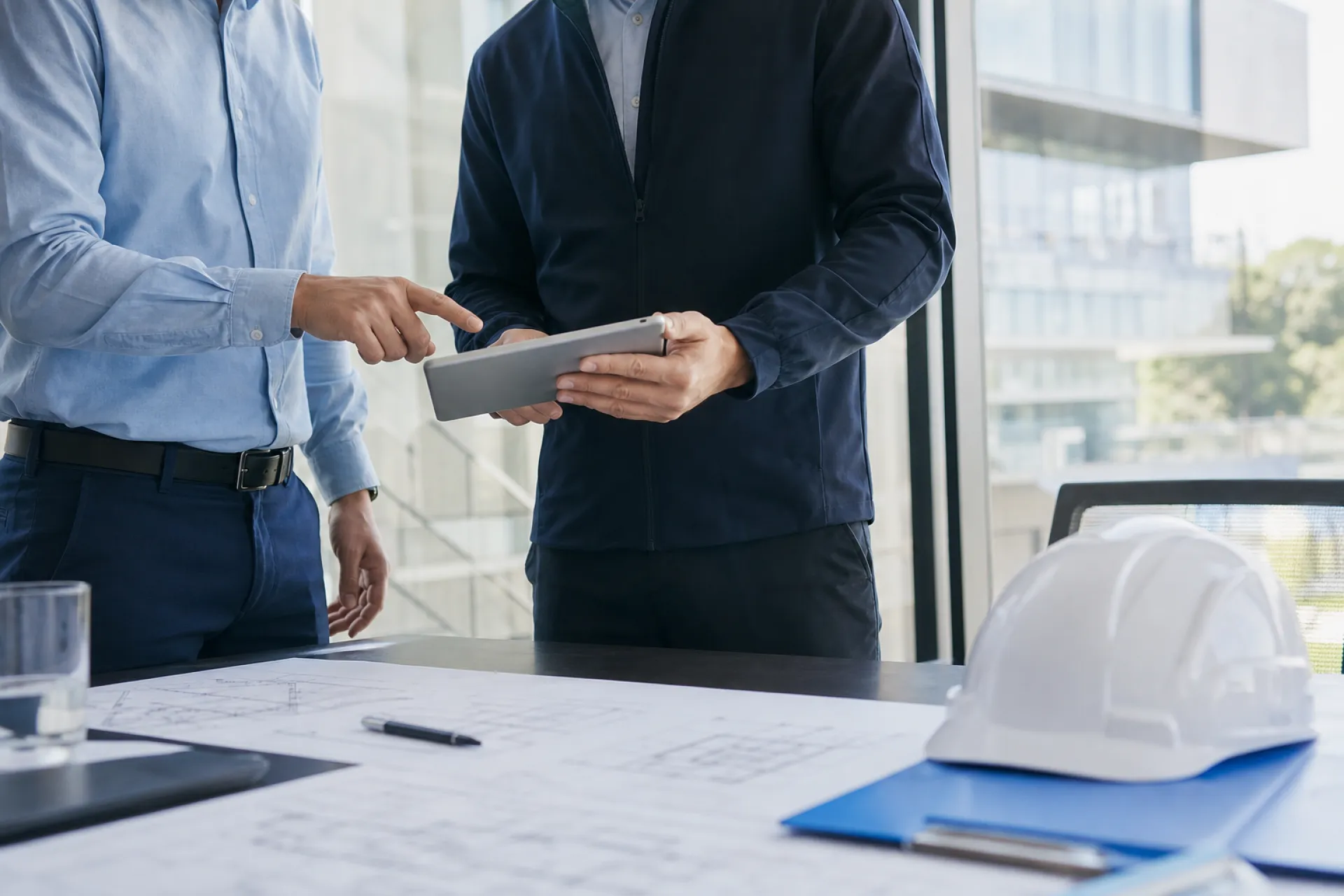 Réunion de suivi de travaux d'ascenseur entre un client et un ascensoriste autour d'une tablette.